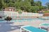 Pheasant Run Apartments | Enjoy the outdoor swimming pool at Pheasant Run Apartments in Nashua NH, featuring turquoise lounge chairs and tables, a white fence, tall green trees, umbrellas, and potted plants under a clear blue sky. | Apartments with Washer & Dryer in Nashua