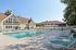 Pheasant Run Apartments | Two teal lounge chairs sit under a white pergola beside a swimming pool at Pheasant Run Apartments, with a large, light-colored building and trees in the background on a sunny day in Nashua NH. | Nashua Apartments with Virtual Tours