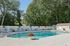 Pheasant Run Apartments | A large, modern house with tall windows and a gabled roof stands behind an outdoor swimming pool at Pheasant Run Apartments. Lounge chairs and plants are arranged along the poolside under a clear blue Nashua NH sky. | Apartments with Balcony in Nashua