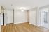 Princeton Properties | A bright, empty room at Brookstone Manor Apartments in Milford, New Hampshire features light gray walls, wood-style flooring, white trim, a hallway, double closet doors, a ceiling light fixture, and an open doorway to another room with mirrored closet doors. | Apartments with Washer & Dryer in Milford