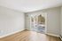 Princeton Properties | A bright, empty room at Brookstone Manor Apartments in Milford, New Hampshire features light wood flooring, beige walls, a wall-mounted air conditioner, and large sliding glass doors leading to a snowy balcony with trees beyond. | Pet Friendly Apartments in Milford
