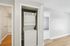 Princeton Properties | A compact laundry area with an in-home washer/dryer is built into a closet with white doors. Nearby are a light-colored hallway, a bathroom with a tub, and a room with neutral walls and carpeting at Brookstone Manor Apartments, Milford New Hampshire. | Apartments with Washer & Dryer in Milford