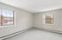 Princeton Properties | A bright, empty room at Brookstone Manor Apartments in Milford, New Hampshire, features beige walls and two large windows letting in natural light. Carpeted floors and white baseboard heaters line the walls, with snowy scenery visible outside. | Pet Friendly Apartments in Milford