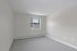 Princeton Properties | Empty room with light gray carpet, beige walls, natural light from a single window, and baseboard heating. This clean, minimalistic space is found at Brookstone Manor Apartments in Milford, New Hampshire. | Apartments with Washer & Dryer in Milford