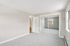 Princeton Properties | Bright, empty bedroom at Brookstone Manor Apartments in Milford, New Hampshire, featuring light gray carpet, beige walls, two windows, a white door, and a large closet with sliding mirrored doors reflecting the opposite window. | Apartments with Air Conditioning in Milford