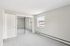 Princeton Properties | A bright, empty room with light gray walls, white trim, carpeted floor, two large windows, a mirrored closet door, and an open door at Brookstone Manor Apartments in Milford New Hampshire. | Milford Apartments with Virtual Tours