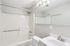 Princeton Properties | This bathroom at Brookstone Manor Apartments in Milford, New Hampshire features a white bathtub and shower combo, a toilet, and a white sink with silver faucet. A large mirror and three-light fixture sit above the sink. Walls are light gray. | Apartments with Washer & Dryer in Milford