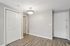 Princeton Properties | A bright, empty room at Brookstone Manor Apartments in Milford, New Hampshire, featuring light gray walls, wood-style flooring, a double-door closet, a white entry door, and a modern ceiling light fixture. | Apartments with Air Conditioning in Milford
