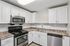 Princeton Properties | Modern kitchen with white cabinets, stainless steel appliances including a stove, microwave, and dishwasher, marble-patterned countertops, tiled backsplash, and a double sink under bright ceiling lighting at Brookstone Manor Apartments in Milford New Hampshire. | Apartments with Air Conditioning in Milford