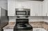 Princeton Properties | A modern kitchen at Brookstone Manor Apartments in Milford, New Hampshire features white cabinets, a stainless steel microwave above a black electric stove with coil burners, and a marble-patterned countertop set against a white tile backsplash. | Pet Friendly Apartments in Milford