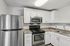 Princeton Properties | Modern kitchen at Brookstone Manor Apartments in Milford, New Hampshire, featuring white cabinets, a stainless steel refrigerator, built-in microwave, electric stove, double sink with marble-patterned countertop, tile backsplash, and wood-style flooring. | Apartments with Washer & Dryer in Milford