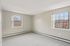 Princeton Properties | A bright, empty room at Brookstone Manor Apartments in Milford, New Hampshire features beige walls, light gray carpet, and two large windows letting in natural light and showcasing leafless winter trees outside. | Pet Friendly Apartments in Milford
