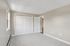 Princeton Properties | Empty bedroom at Brookstone Manor Apartments in Milford, New Hampshire, featuring light gray carpet, beige walls, two windows, a double-door white closet, and an open door to the hallway. The room is bright with natural light. | Apartments with Washer & Dryer in Milford