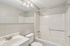 Princeton Properties | A clean, modern bathroom at Brookstone Manor Apartments in Milford, New Hampshire features a white sink, silver faucet, toilet, and bathtub-shower combo. A large mirror and three-bulb vanity light fixture sit above the sink. | Milford Apartments with Virtual Tours