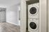 Princeton Properties | A white in-home washer/dryer is neatly stacked in a small closet with the door open, beside a hallway with wood flooring and light gray walls at Brookstone Manor Apartments in Milford, New Hampshire. An air conditioning unit is on the adjacent wall. | Apartments with Air Conditioning in Milford