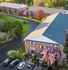 Aerial view of charming brick apartment complexes surrounded by lush trees and vibrant blossoms, featuring well-maintained pathways and a spacious parking area.