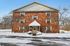Inviting brick apartment building with a snow-covered landscape and accessible parking spaces, ideal for winter living.