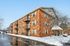 Charming brick apartment building with balconies, surrounded by snow-covered ground and clear skies, offering a cozy and picturesque living environment.