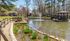 Charming outdoor view of a serene pond with a fountain and a picturesque wooden bridge surrounded by lush greenery and blooming trees.| The Royal Crest | Apartment in North Andover, MA