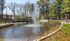 Serene park setting with a picturesque pond, elegant fountains, and a charming wooden bridge surrounded by lush greenery.| The Royal Crest | Apartment in North Andover, MA