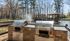Charming outdoor space featuring sleek stainless steel grills and a tranquil pond with a picturesque wooden bridge.| The Royal Crest | Apartment in North Andover, MA