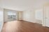 Bright and spacious living area with sleek hardwood flooring, large sliding glass doors opening to a private balcony, and a cozy adjoining room, offering a chic and inviting setting.| Village Green | Apartment in Tewksbury, MA