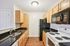 Modern kitchen with elegant granite countertops, sleek black appliances, and warm wooden cabinetry.| Village Green | Apartment in Tewksbury, MA