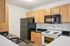 Modern kitchen with sleek black granite countertops, stylish wooden cabinets, and essential appliances including a refrigerator, stove, and microwave.| Village Green | Apartment in Tewksbury, MA