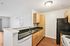 Modern kitchen with sleek black countertops, light wood cabinets, and a spacious open layout leading into the living area.| Village Green | Apartment in Tewksbury, MA