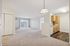 Bright and spacious living area with plush carpeting, featuring an open-plan design and modern kitchen with wood finish cabinets.| Village Green | Apartment in Tewksbury, MA