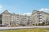 Charming beige apartment complex with multiple balconies, ample parking, and lush surroundings under a clear blue sky. | Village Green | Tewksbury Apartments