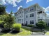 Beautiful three-story apartment building with classic architecture, surrounded by lush landscaping and a serene bench, under a vibrant blue sky.