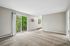Bright and airy living room with plush carpet, large windows, and sliding glass doors opening to a lush green balcony view.