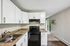 Modern kitchen with sleek white cabinetry, granite countertops, and a stainless steel sink, leading to a bright open living space with large sliding doors.