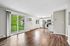 Bright and modern open-concept living space featuring a sleek kitchen with stainless steel appliances and elegant wood flooring, overlooking lush greenery through large glass doors.
