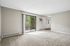 Bright and airy living room with plush carpeting, large sliding glass door opening to a charming balcony, featuring serene outdoor views and abundant natural light.