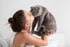 Charming moment of a woman lovingly embracing a fluffy gray cat in a serene bedroom setting.