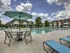 Resort-style swimming pool at Kelly&rsquo;s Ridge Apartments in Columbia, MO, with lounge chairs, a shaded table and chairs, and surrounding red-brick apartment buildings under a bright blue sky with scattered clouds.