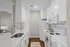 Chic and modern kitchen with white cabinetry, sleek countertops, and stainless-steel features on a warm wooden floor.