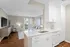 Elegant open-concept apartment featuring a modern kitchen with pristine white cabinetry and a cozy living area leading to a sunlit balcony.