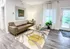 Chic living room with modern gray sofa, glass coffee table on a stylish rug, and abundant natural light from large windows.