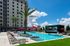 Luxurious outdoor pool area with stylish loungers, red umbrellas, and a large screen, set against a modern apartment building and clear blue skies.