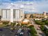 Dynamic aerial view of a modern urban apartment complex with ample parking and lush greenery, offering a vibrant city lifestyle.
