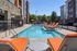 Inviting apartment complex pool area with vibrant orange cushioned sun loungers and modern brick architecture.