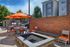 Chic outdoor patio featuring a modern fire pit, stylish seating with vibrant orange cushions, and a barbecue area under sunny skies.