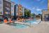 Inviting apartment complex with a luxurious pool and vibrant orange lounge chairs, perfect for relaxation under a clear blue sky.