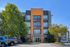Modern apartment building with eye-catching orange accents, surrounded by lush greenery and a vibrant parking area.