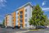 Modern apartment complex with vibrant orange accents and ample parking, framed by lush greenery under a clear blue sky.