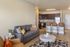 Contemporary open-concept living space featuring a cozy gray sofa, stylish kitchen with modern appliances, and elegant bar stools, perfect for comfortable living and entertaining.