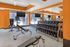Modern gym with bright orange walls, featuring state-of-the-art cardio equipment, free weights, and a view of the outdoor pool.
